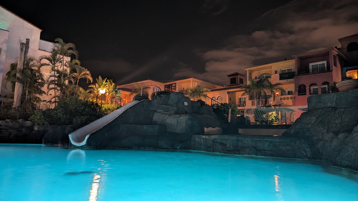 Beleuchteter Pool mit Wasserrutsche und Palmen auf Teneriffa bei Nacht